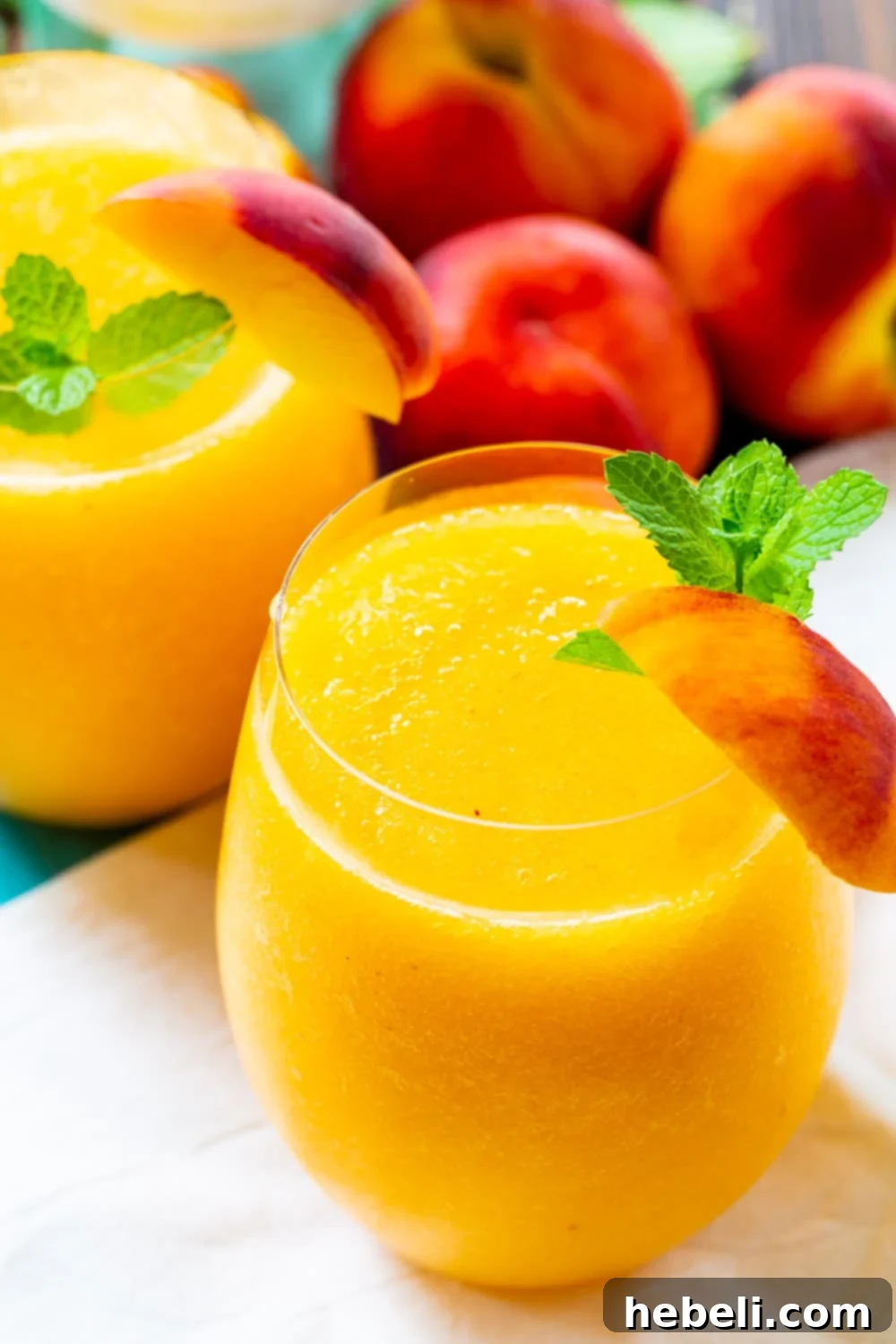 Three Peach Wine Slushies surrounded by fresh peach halves, showcasing their vibrant color and refreshing appeal.