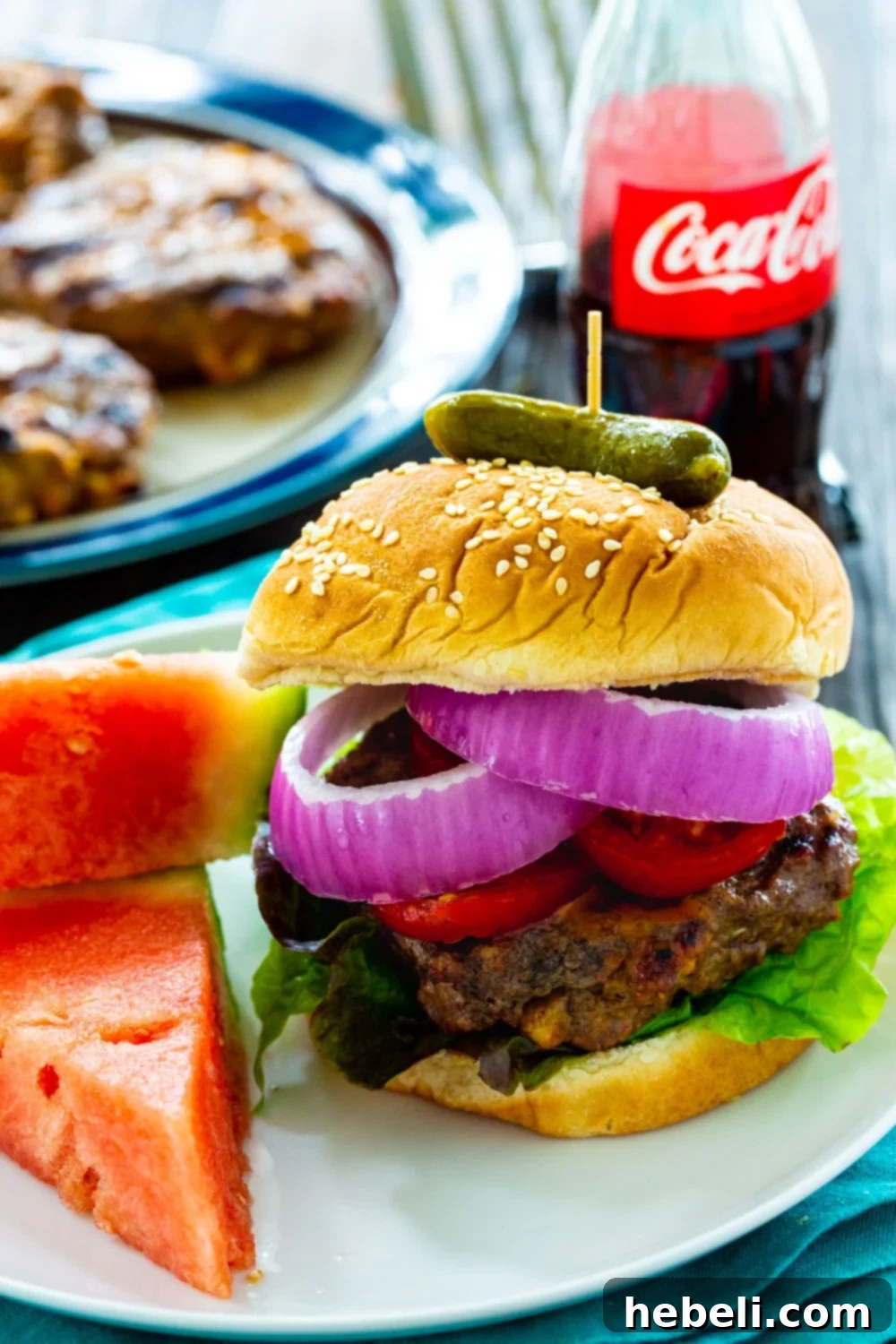 A delicious Cola Burger served on a plate next to fresh watermelon slices, ready for a summer meal.
