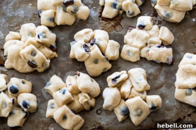 Small mounds of blueberry-filled dough rising on a greased baking sheet, covered with a kitchen towel.