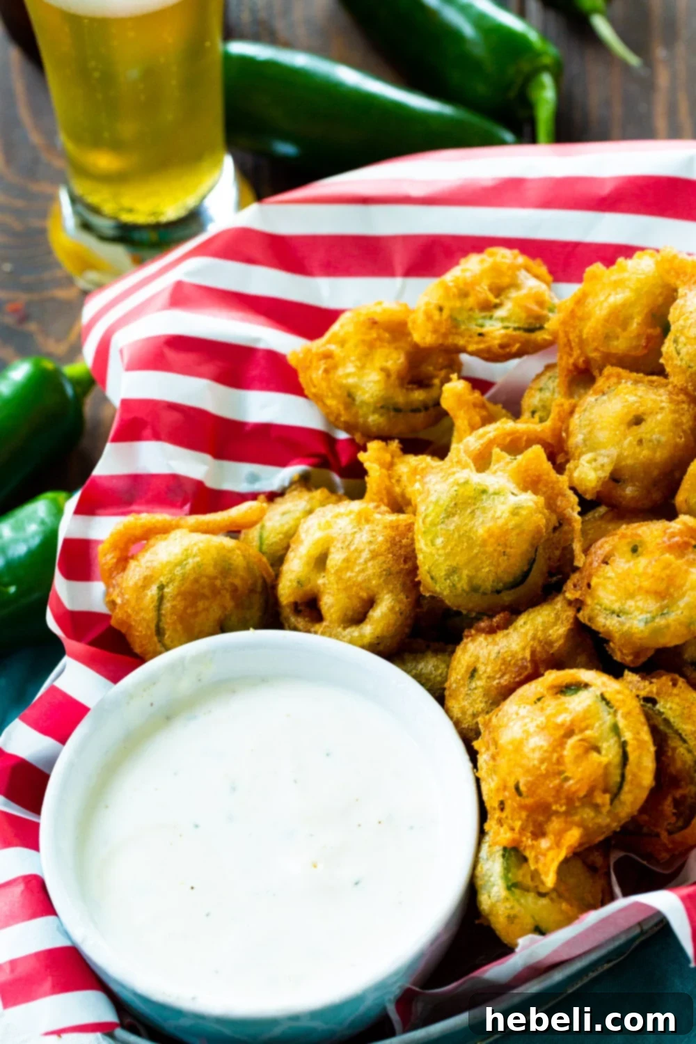 A basket full of golden-brown Fried Jalapenos, surrounded by fresh, green jalapeno peppers.