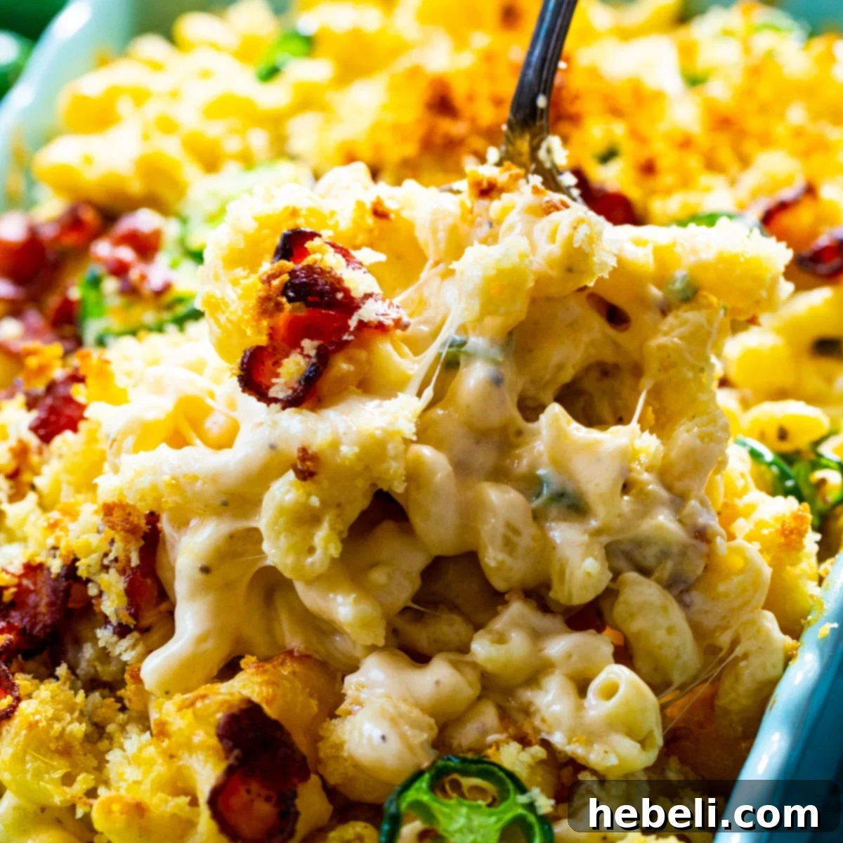 A serving spoon scooping a generous portion of golden-brown Jalapeño Popper Mac and Cheese, showcasing the creamy texture, crispy bacon bits, and vibrant green jalapeño pieces within.