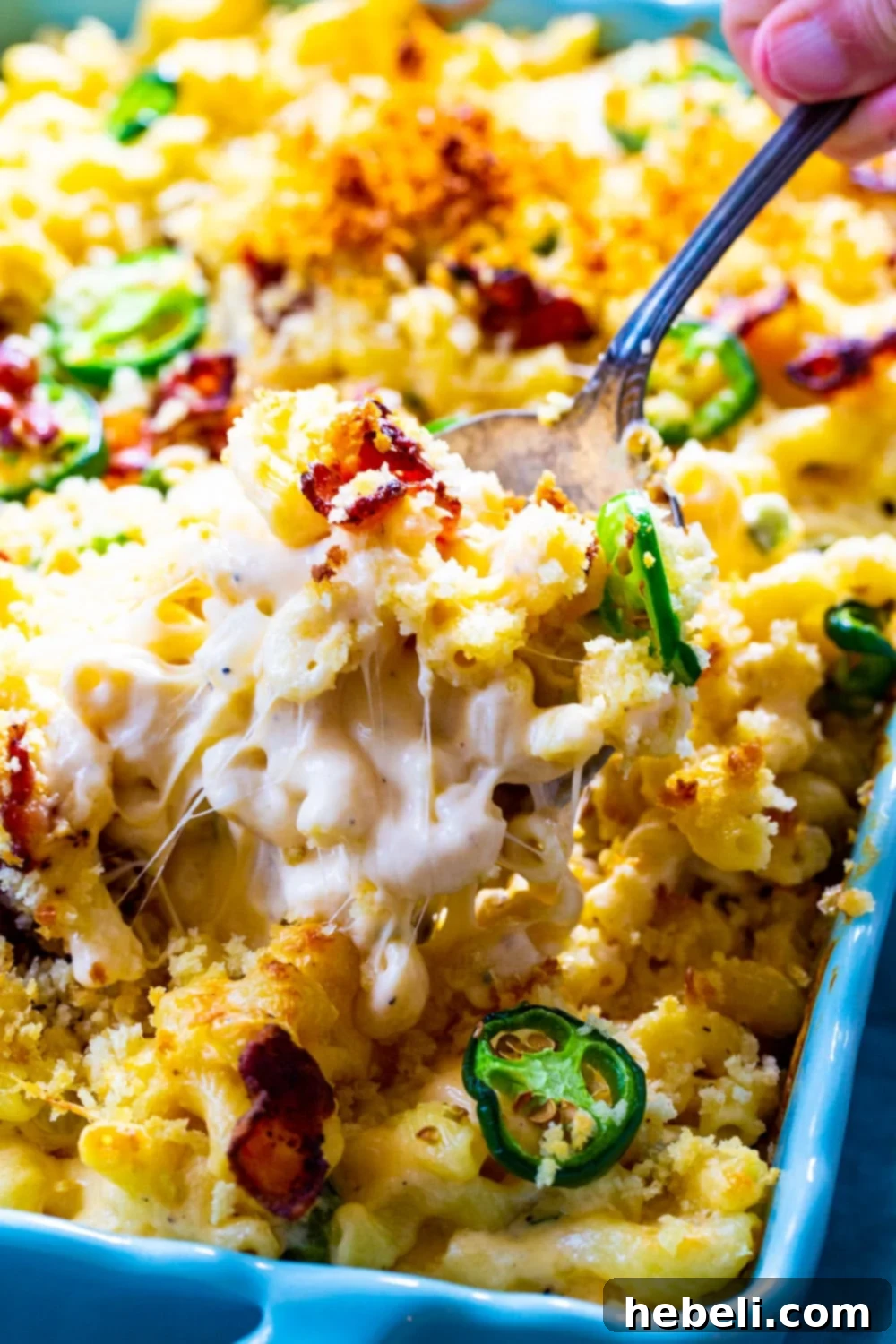 Close-up of a spoon lifting a generous portion of creamy and cheesy Jalapeño Popper Mac and Cheese from a baking dish, showing the texture and the golden Panko topping.
