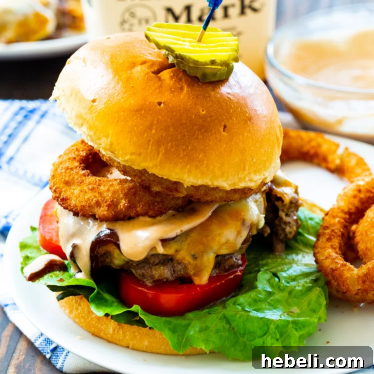 Close-up of a Bourbon BBQ Burger piled high with crispy fried onion rings, melted Colby Jack cheese, and a rich BBQ mayo, showcasing its delicious layers.