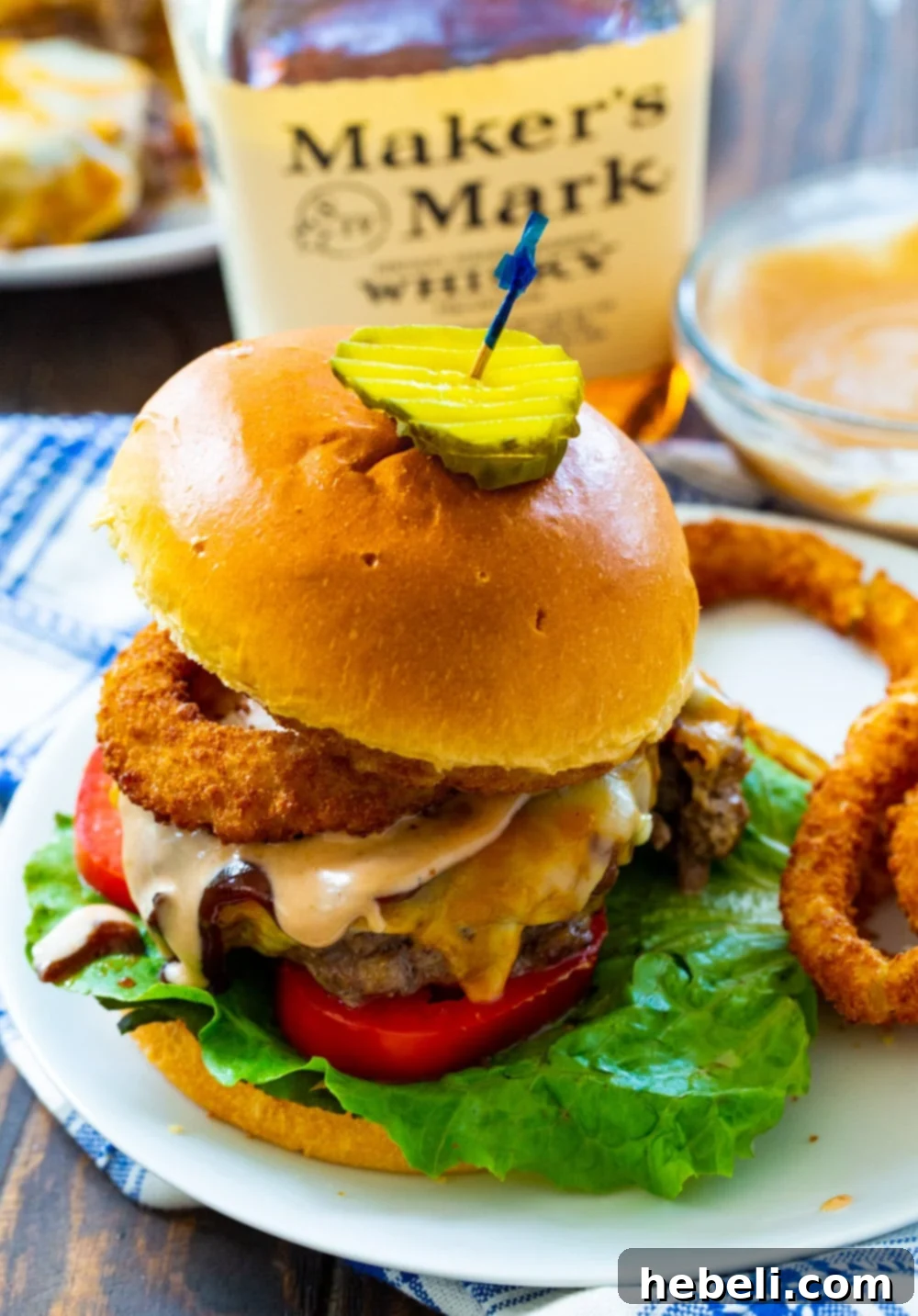 A perfectly cooked Bourbon BBQ Burger with melted cheese, served alongside a pile of golden onion rings on a rustic plate.