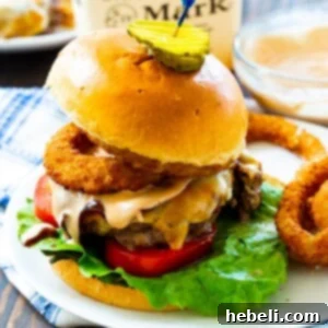 A prepared Bourbon BBQ Burger, topped with onion rings, melted cheese, and fresh ingredients, ready to be served.