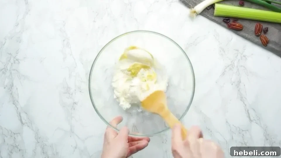 Mixing together softened cream cheese, creamy mayonnaise, and zesty Dijon mustard in a bowl until smooth and well combined.
