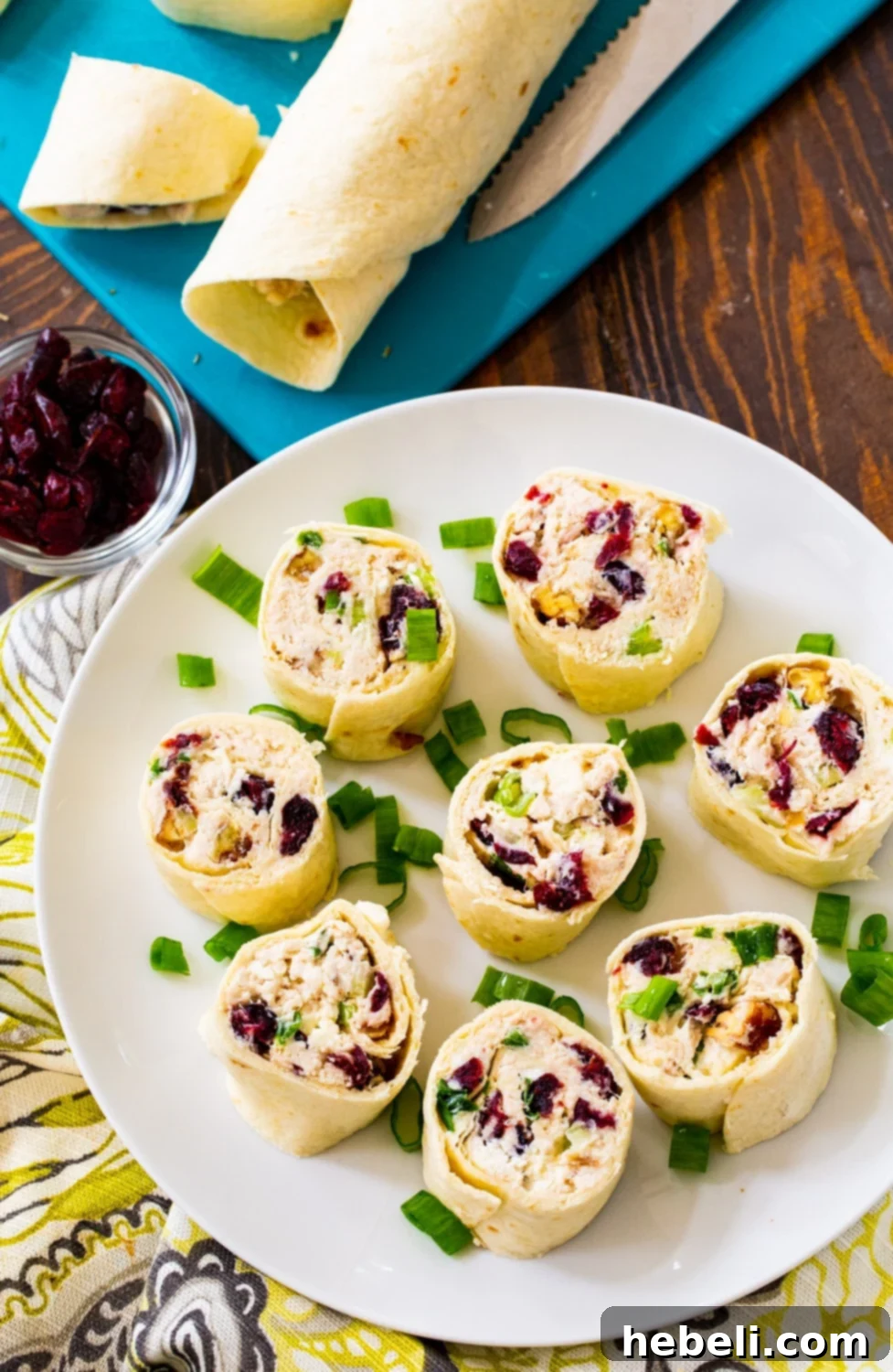 Beautifully cut Chicken Cranberry Pinwheels arranged on a serving plate, with additional uncut tortilla rolls waiting on a cutting board in the background.