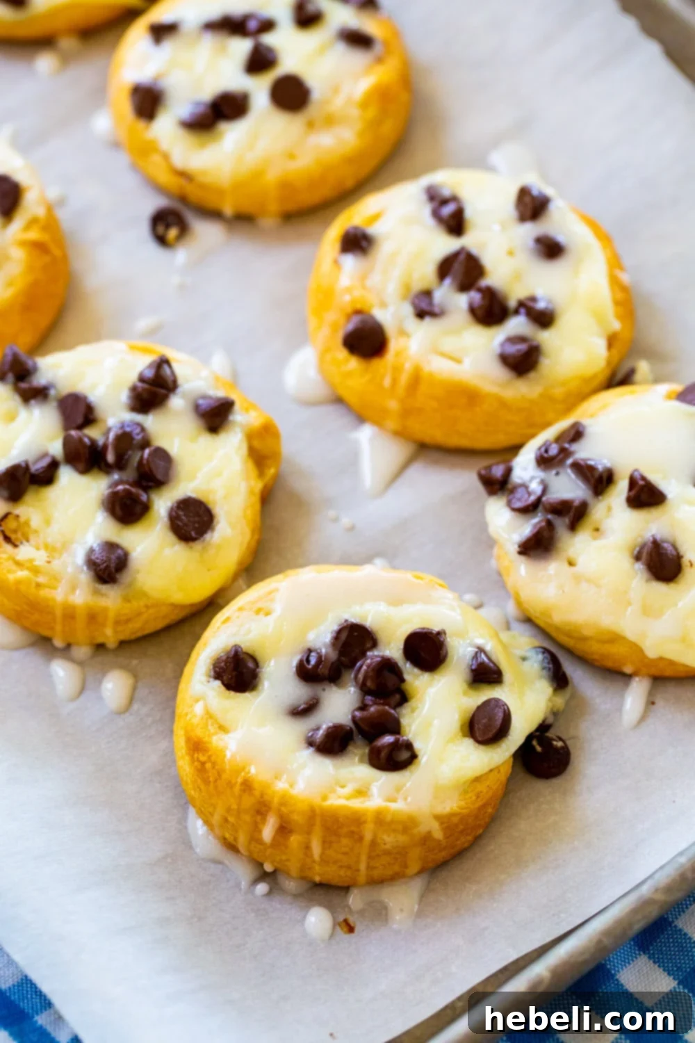 Several freshly baked Chocolate Chip Cream Cheese Danishes cooling on parchment paper, showcasing their inviting golden crust.