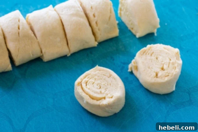 Unrolled crescent roll dough being expertly cut into uniform slices on a cutting board, ready for shaping.