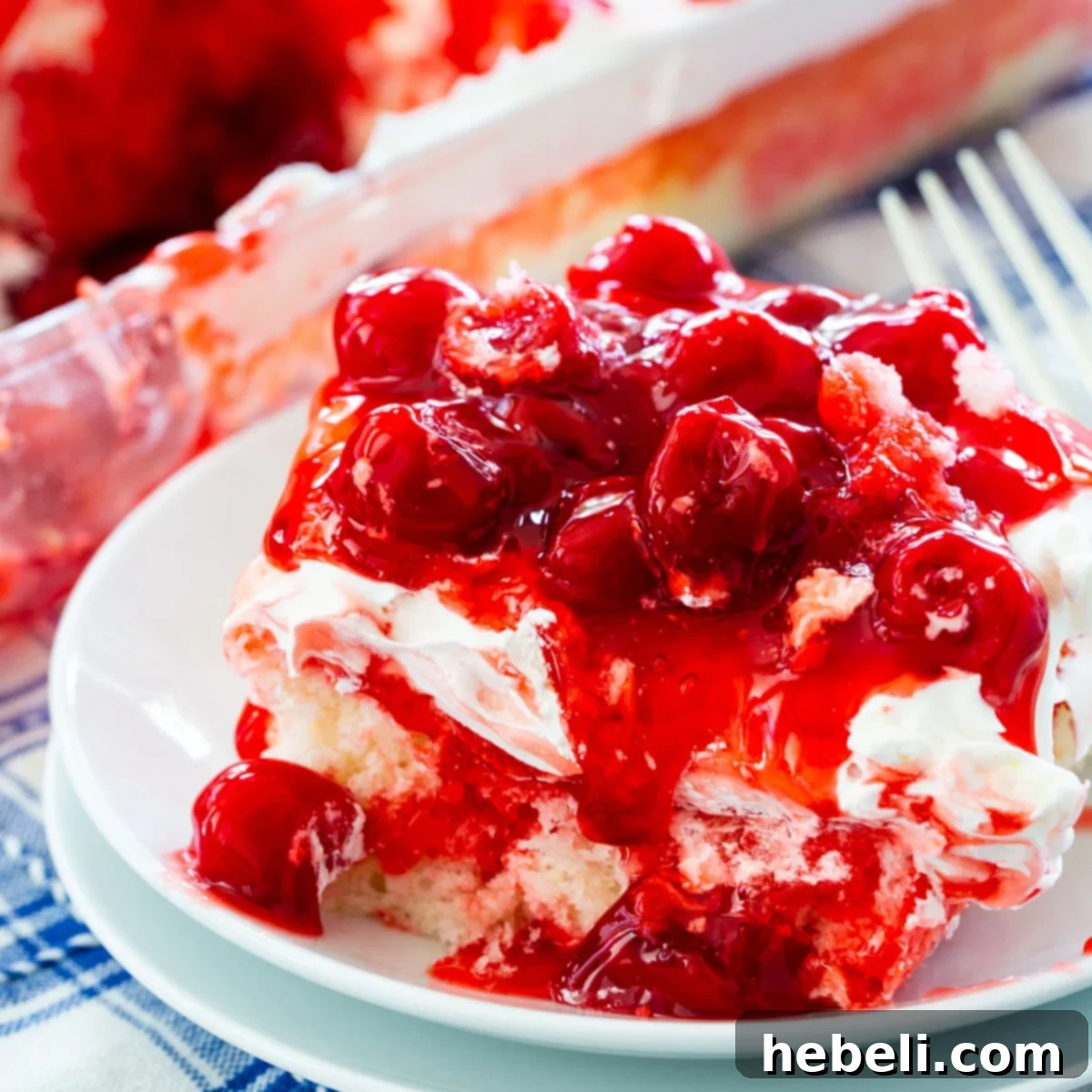 A delectable slice of Cherry Poke Cake, showcasing its moist texture and generous topping of glossy red cherries.
