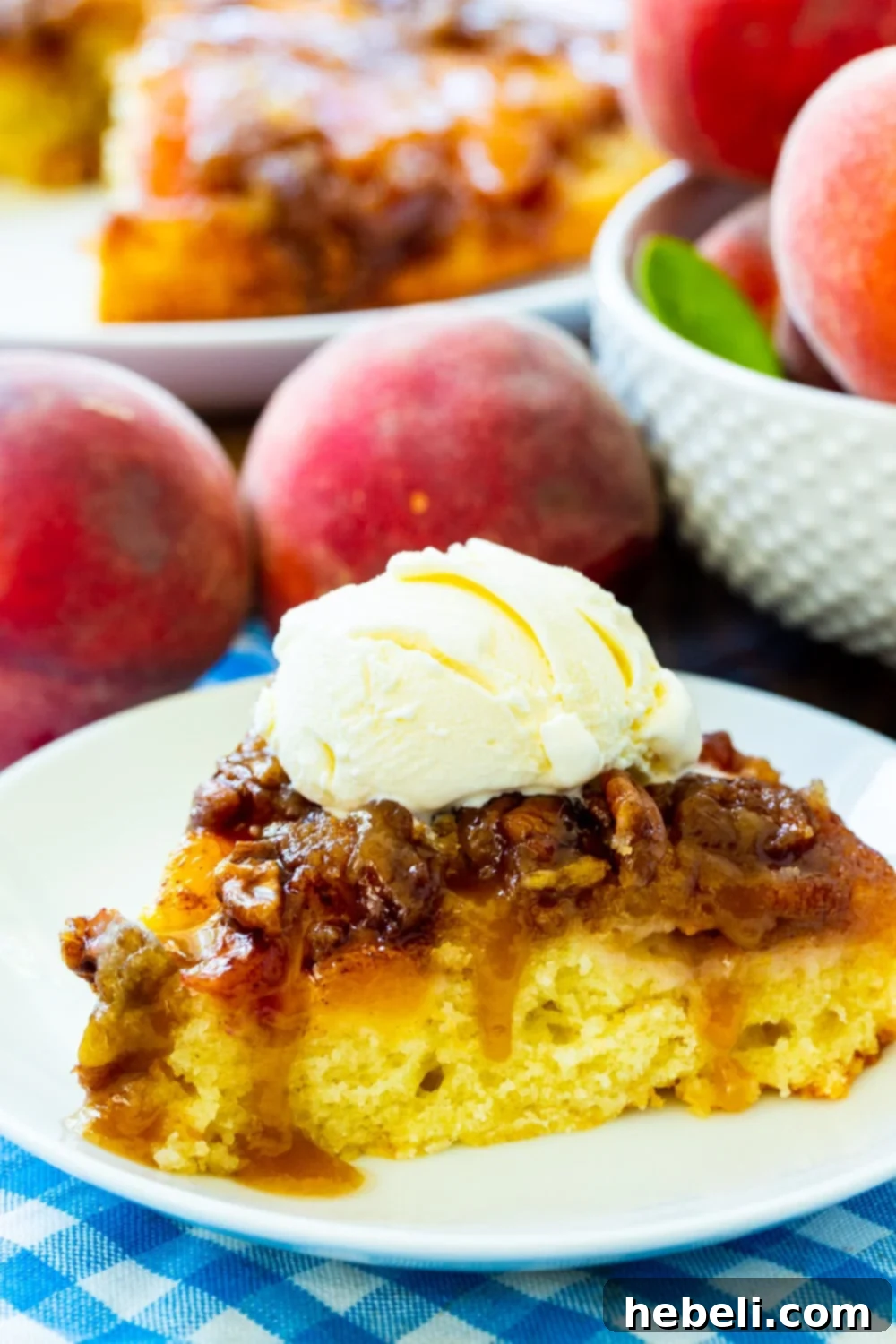 A close-up view of a slice of Peach Praline Upside Down Cake, highlighting its juicy peach topping, crunchy pecans, and moist cake, with fresh peaches scattered around.