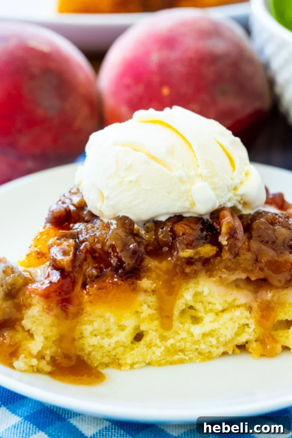 An enticing close-up of a slice of Peach Praline Upside Down Cake, richly topped with melting vanilla ice cream, promising a decadent dessert.