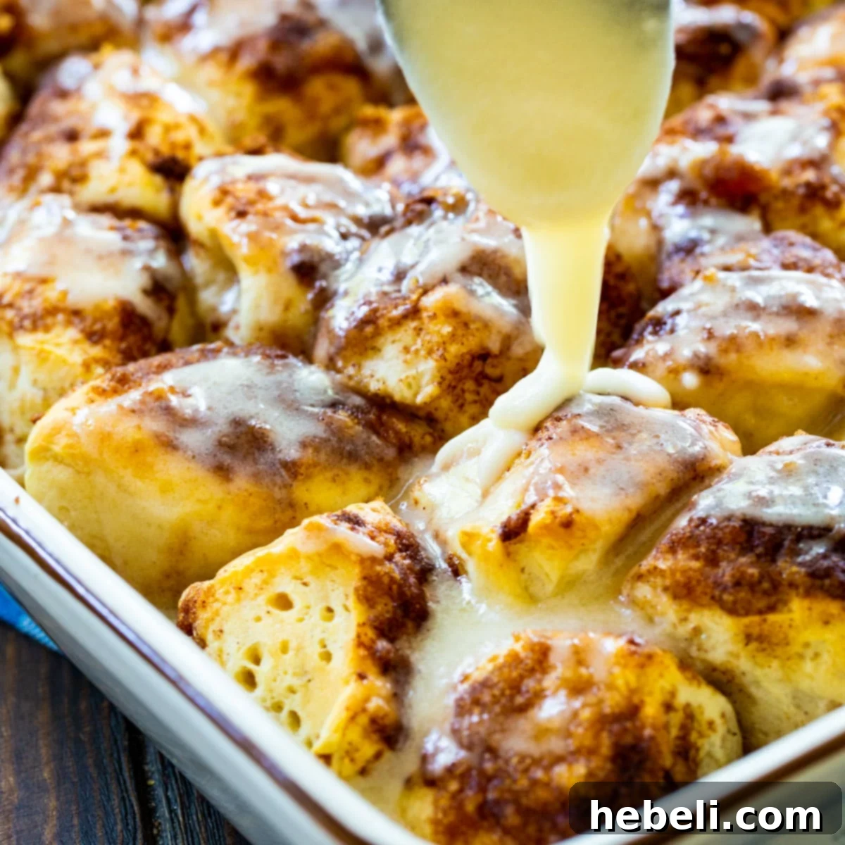 Quick Cinnamon Roll Poppers 2 Spoon drizzling icing on warm Cinnamon Roll Bites in a baking dish