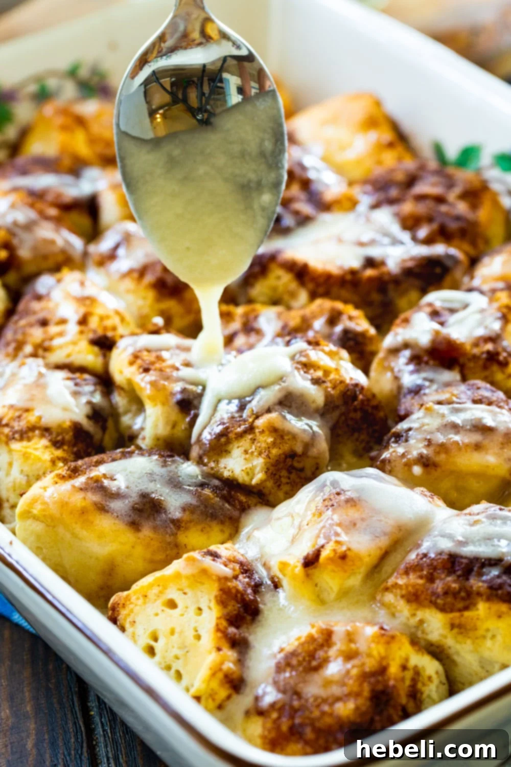 Quick Cinnamon Roll Poppers 3 Close-up of a spoon drizzling vanilla icing over baked cinnamon roll pieces