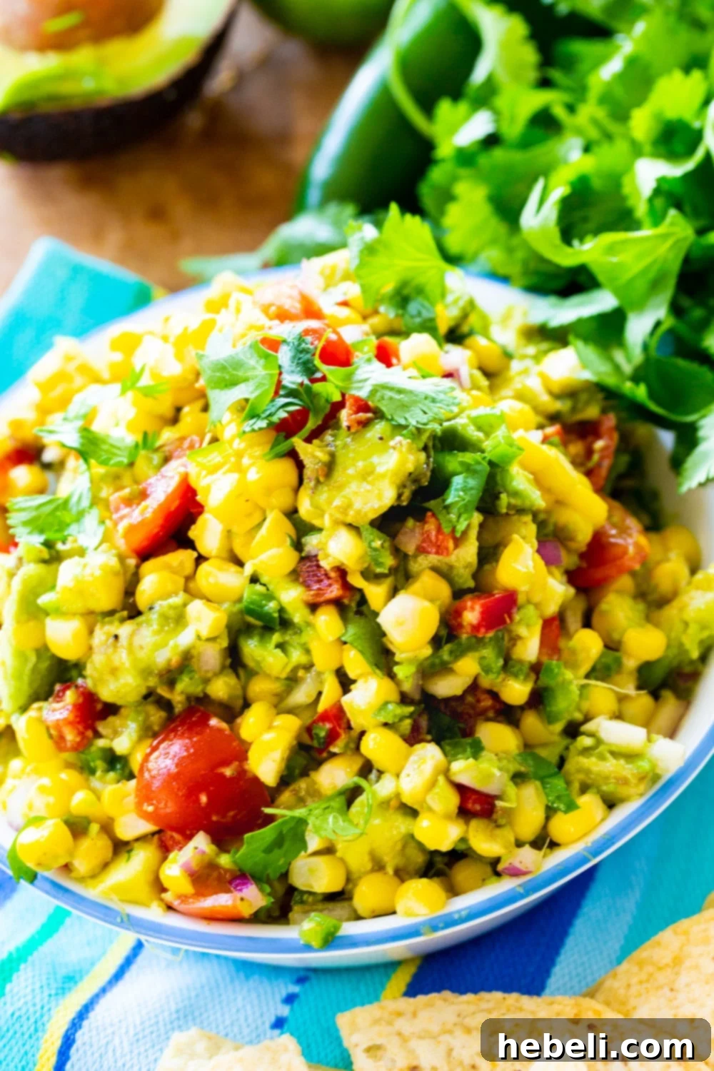 A bowl of freshly made Avocado Corn Salsa, with a bunch of vibrant green cilantro positioned beside it, highlighting its fresh ingredients.