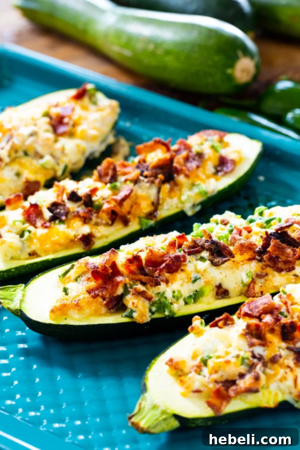 Jalapeno Popper Zucchini Boats on baking sheet with fresh zucchini in background.