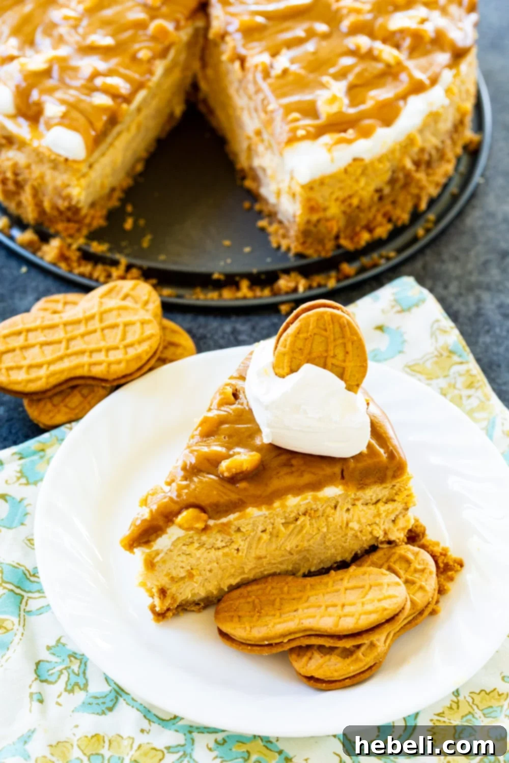 Decadent Peanut Butter Cheesecake 3 Whole Peanut Butter Cheesecake with a slice removed, displaying the creamy filling, marshmallow layer, and glossy peanut butter glaze on a rustic wooden surface.