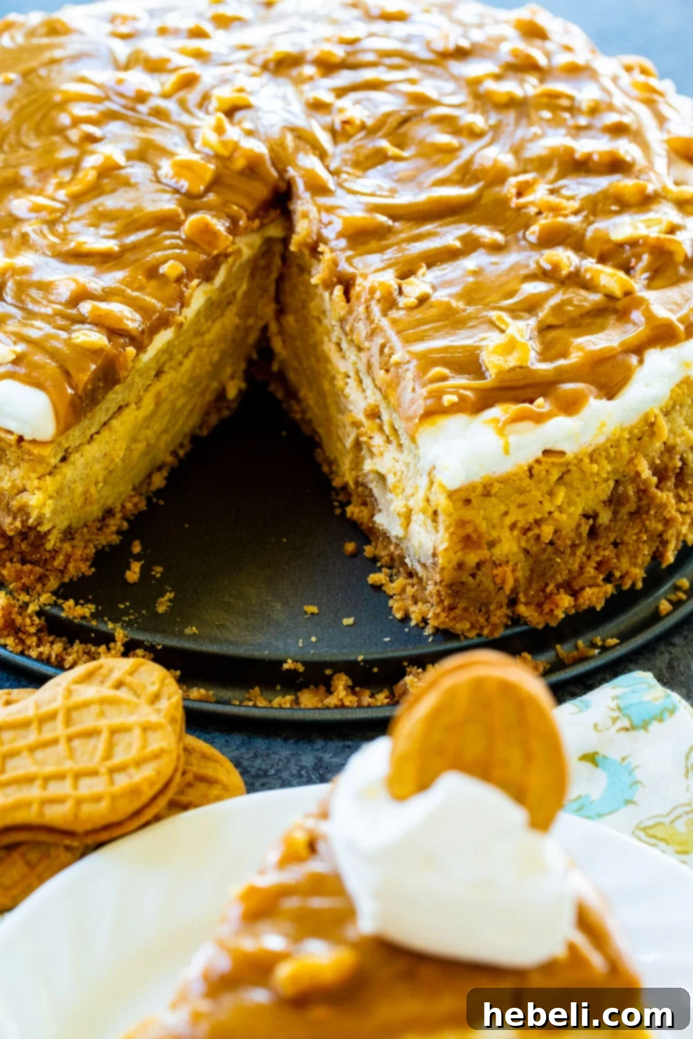 Decadent Peanut Butter Cheesecake 4 Close-up of a Peanut Butter Cheesecake with a slice cut out, revealing the thick peanut butter filling and crunchy Nutter Butter crust. Topped with glaze and chopped peanuts.