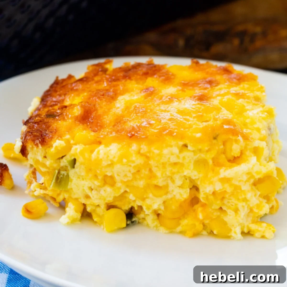 A serving of Three Cheese Corn Pudding on a white plate, showcasing its golden-brown top and creamy interior.
