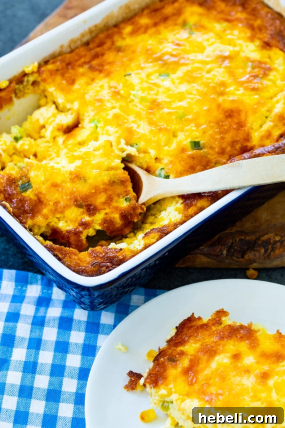 A spoon scooping a generous portion of creamy Three Cheese Corn Pudding from a baking dish.
