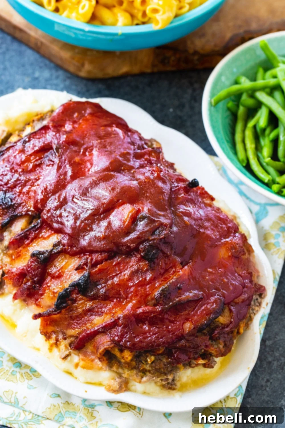 Bacon Enrobed Meatloaf 3 A slice of Bacon Wrapped Meatloaf on a plate, served with a side bowl of fresh green beans, highlighting the delicious glaze.