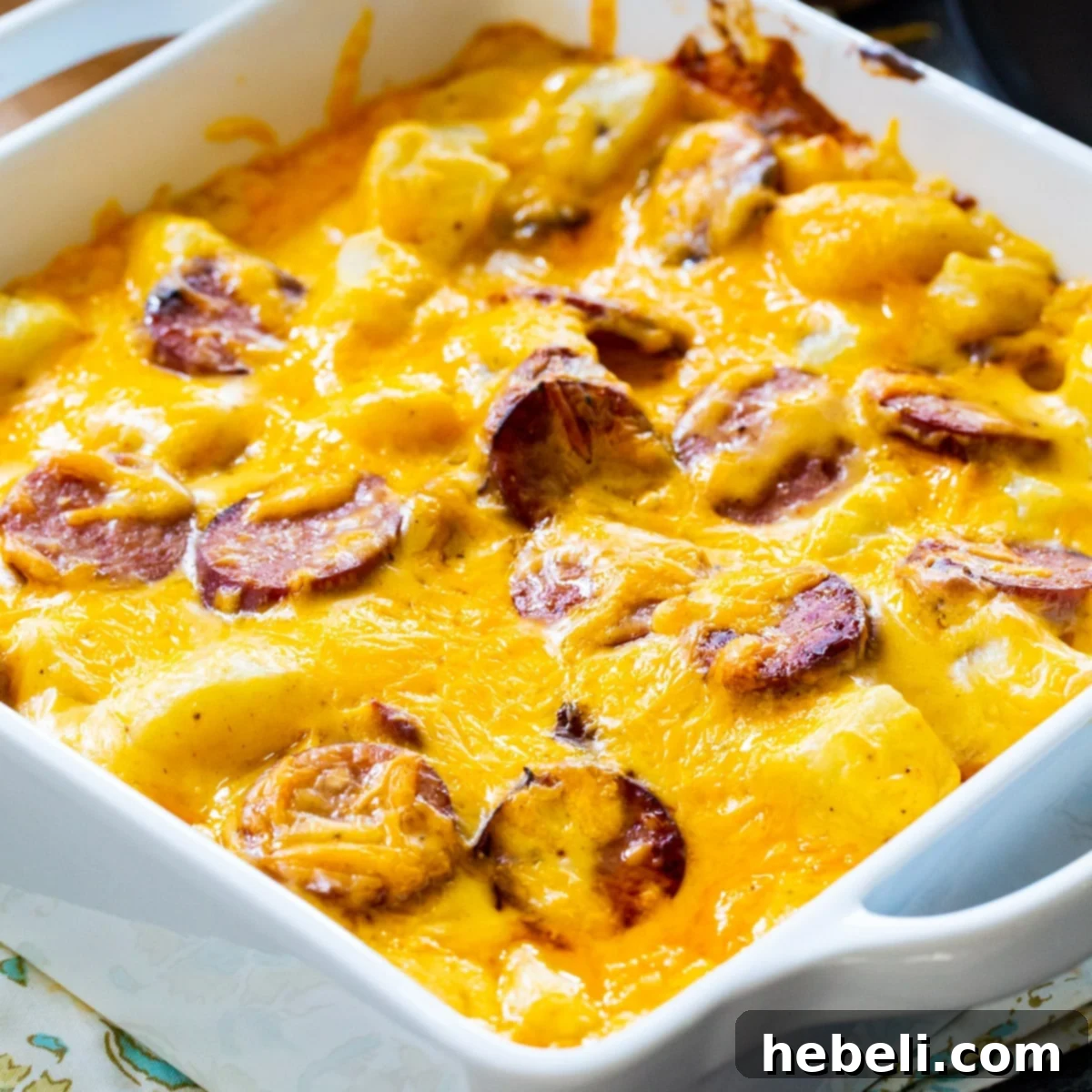 A square baking dish filled with golden-brown Cheesy Potatoes with Smoked Sausage, bubbling with cheese.