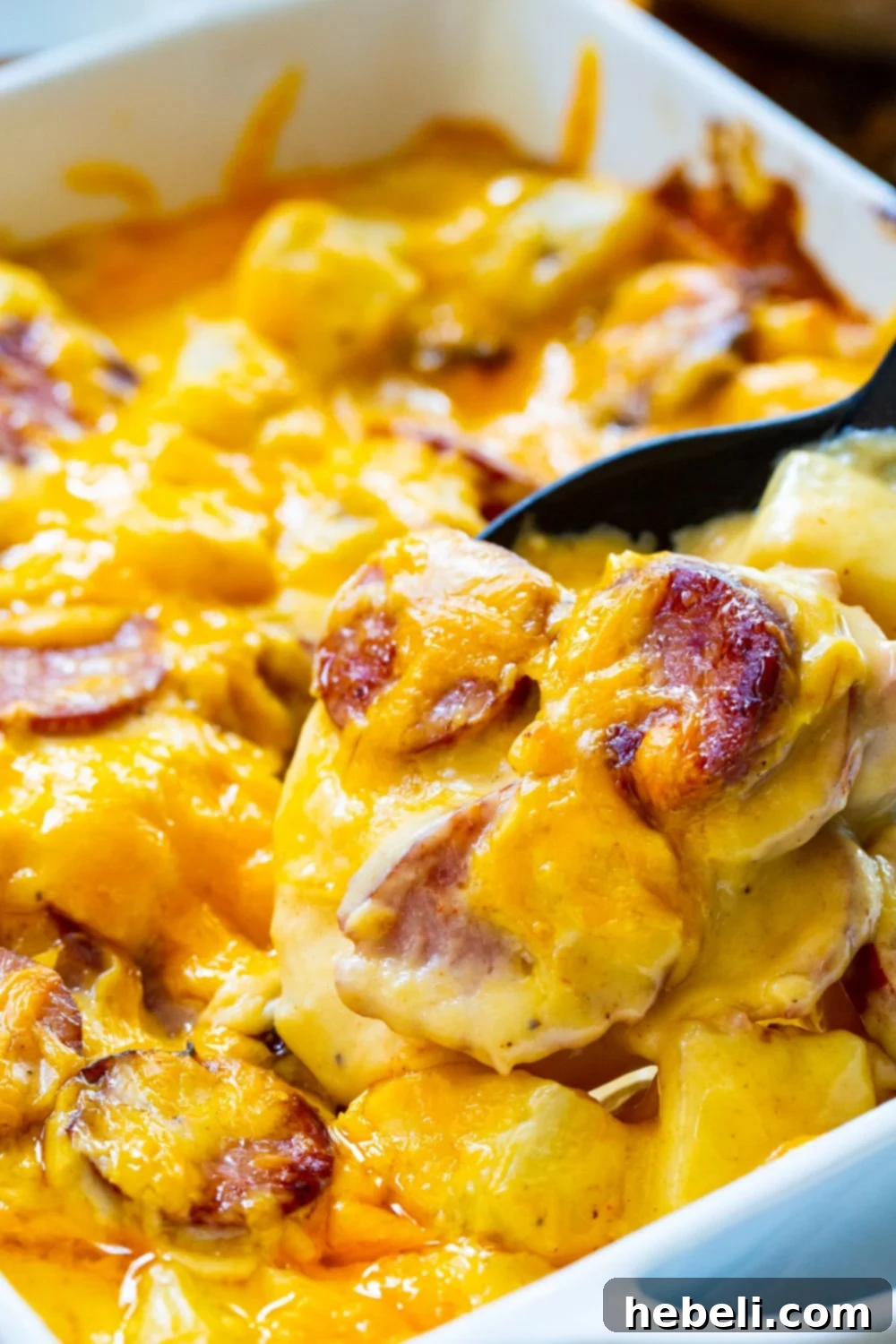 A spoon scooping a generous portion of Cheesy Potatoes with Smoked Sausage from a baking dish, highlighting the creamy texture.