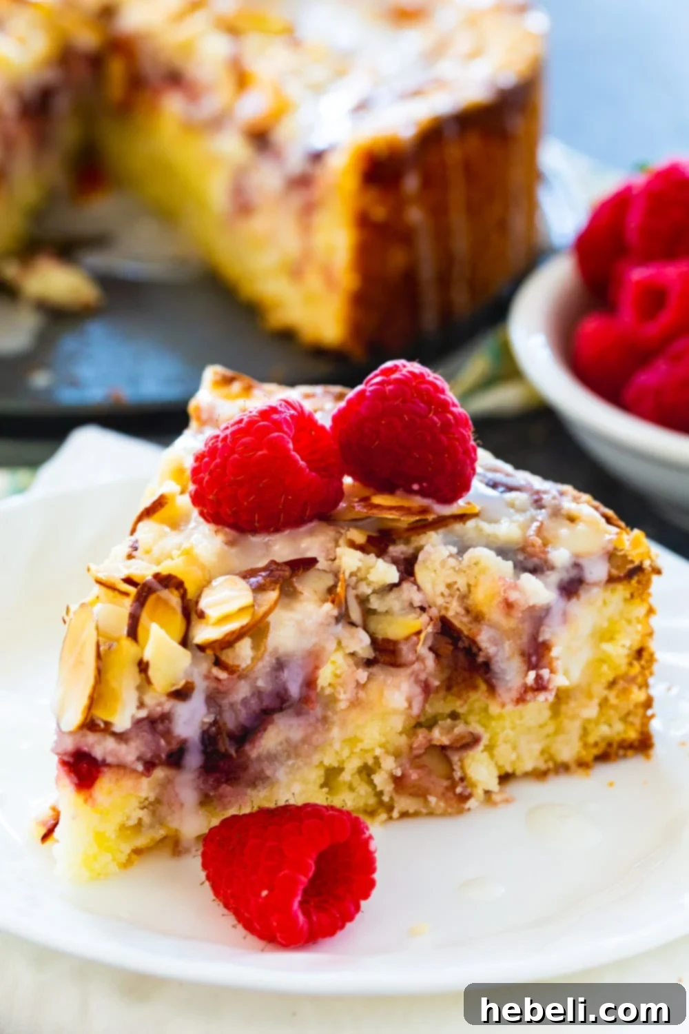 Raspberry Cream Cheese Swirl Coffee Cake 3 A close-up shot of a single slice of Raspberry Cream Cheese Coffee Cake, elegantly topped with fresh, vibrant raspberries, emphasizing its inviting texture and appetizing presentation. Ideal for a festive brunch.