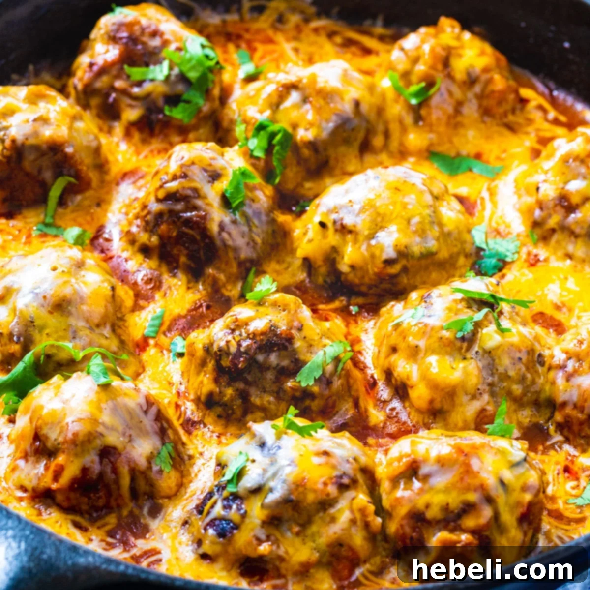 Tex Mex Meatballs coated with melted Mexican cheese and rich enchilada sauce in a rustic skillet, garnished with cilantro.