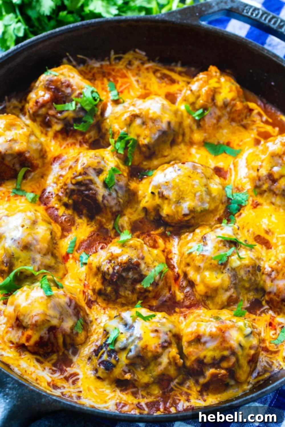 Tex Mex Meatballs simmering in a robust red enchilada sauce within a sturdy cast iron skillet, topped with melting cheese.