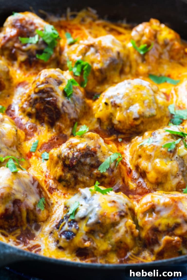 Close-up of Tex Mex Meatballs generously covered in melted cheese and vibrant enchilada sauce, ready to be enjoyed.
