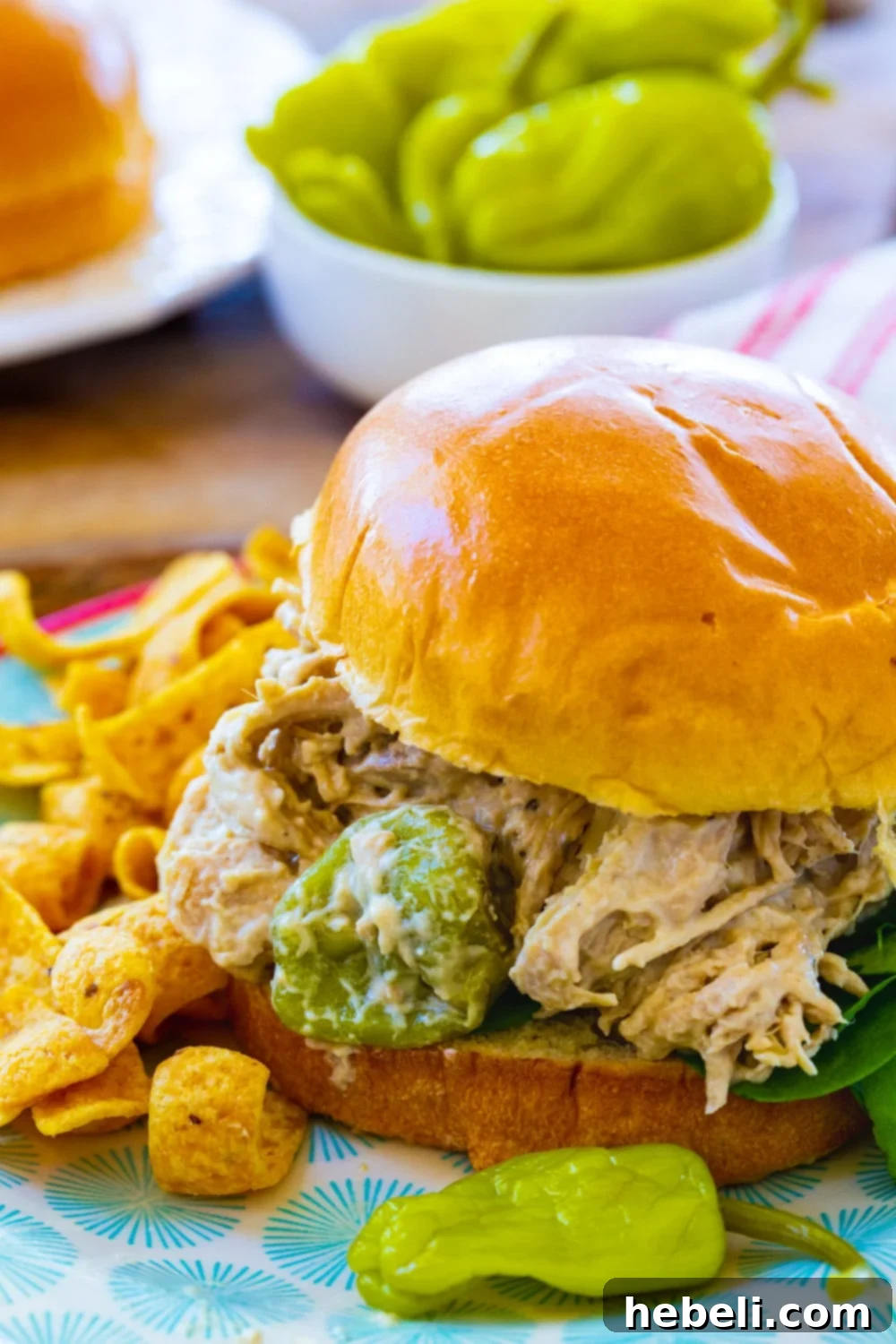 Creamy Mississippi Chicken served on a bun, garnished with a few pepperoncini peppers.