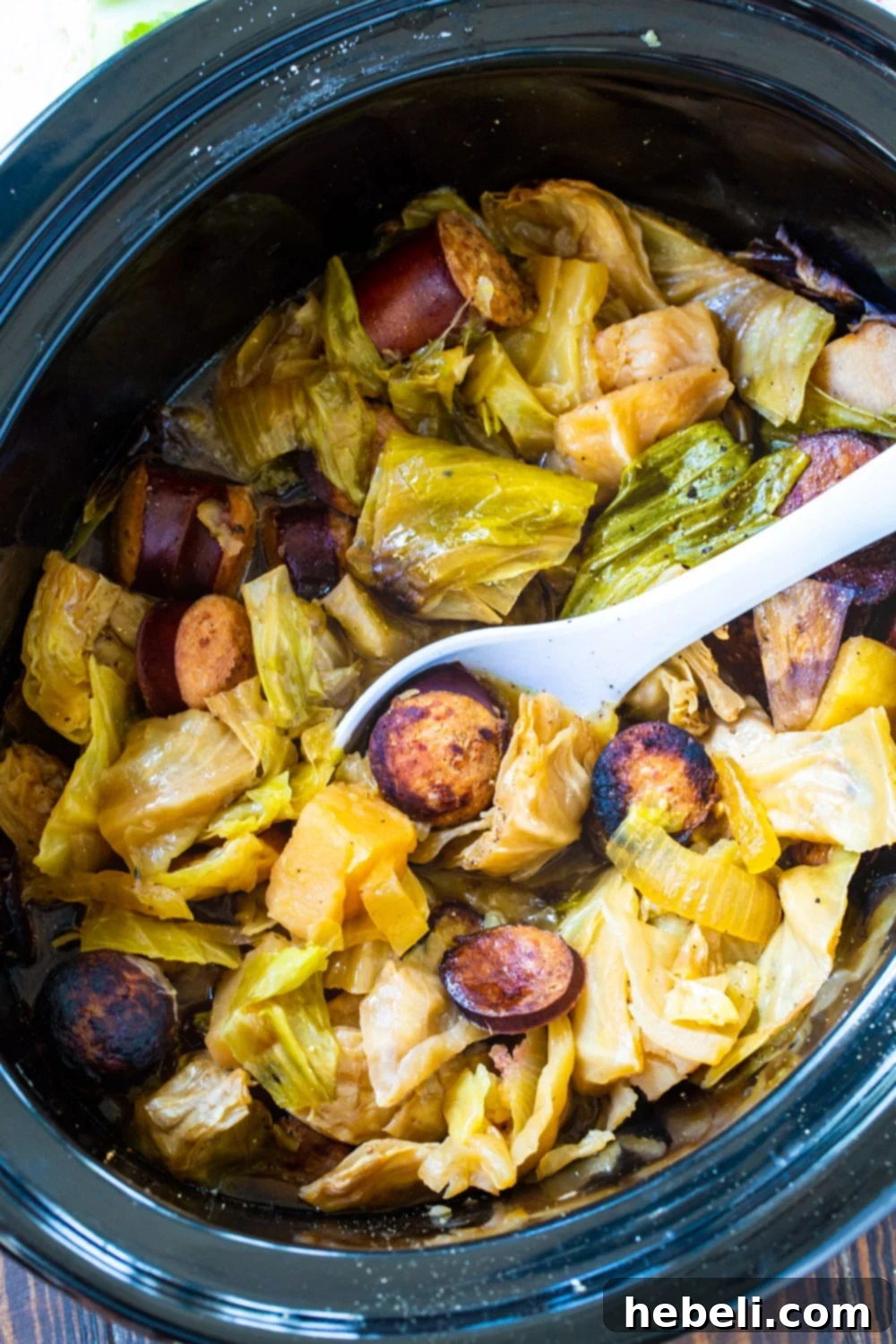 Hearty Slow Cooker Cabbage and Kielbasa 3 Spoon scooping tender cabbage and kielbasa out of slow cooker.