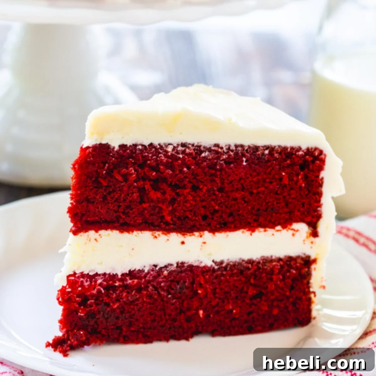 A delectable slice of Red Velvet Cake presented on a pristine white plate, showcasing its vibrant red layers and generous cream cheese frosting.