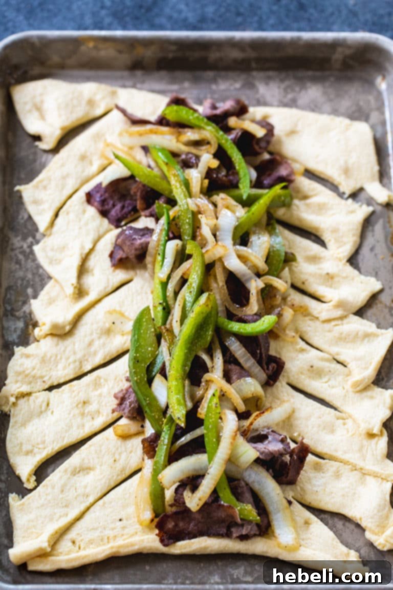 Placing the savory cheesesteak filling onto the unrolled crescent dough, ready for braiding.