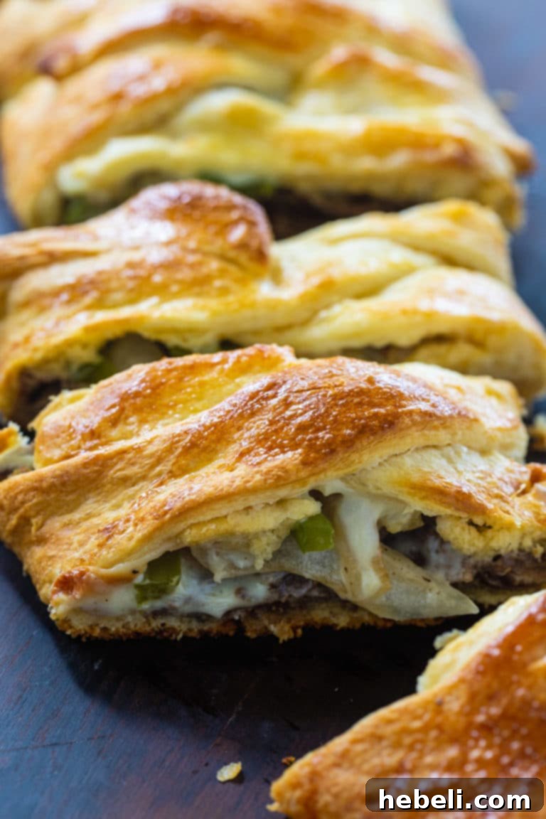 A close-up of a fully assembled and ready-to-bake Cheese Steak Crescent Braid, showing the intricate dough pattern and visible filling of steak, onions, and peppers.