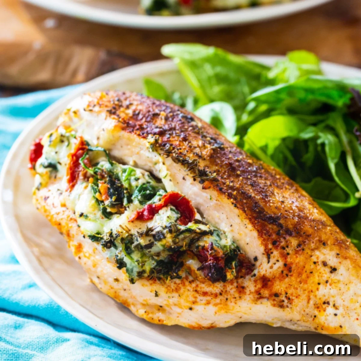 A beautifully cooked Tuscan Stuffed Chicken breast served on a plate with a fresh green salad.