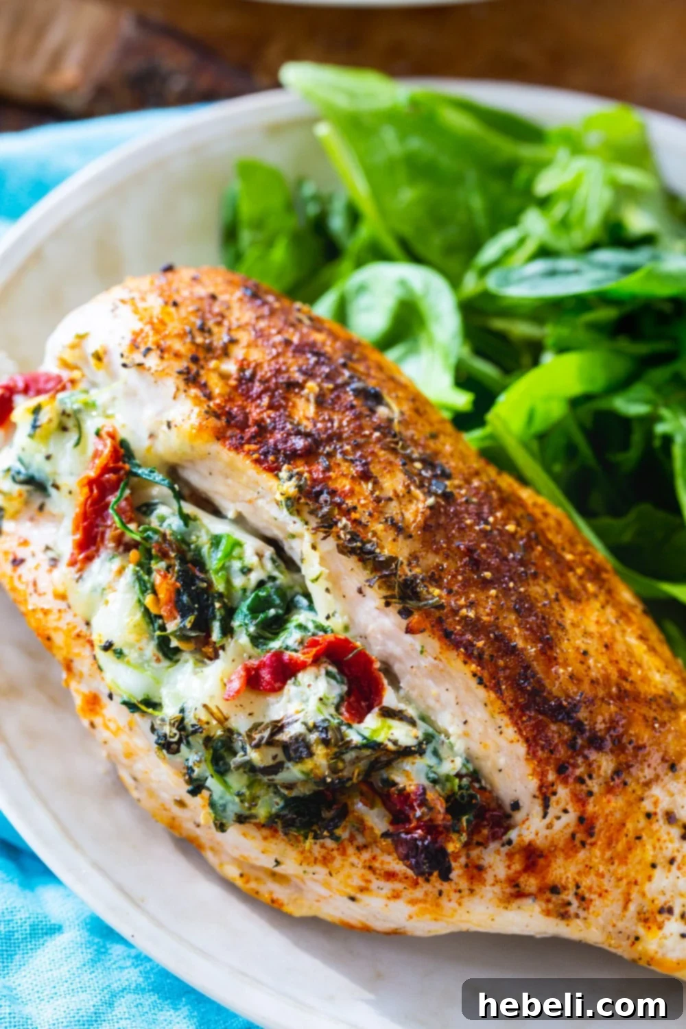 Close-up of a cooked Tuscan Stuffed Chicken breast with its creamy filling visible, served with a side salad.