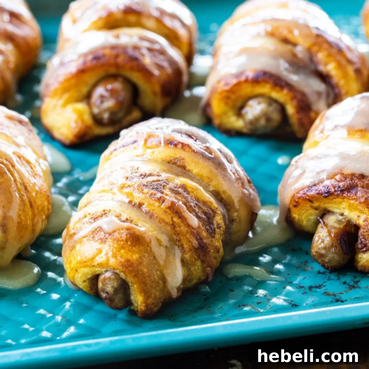 Golden brown Cinnamon Roll Pigs in a Blanket drizzled with icing, served on a blue baking sheet.
