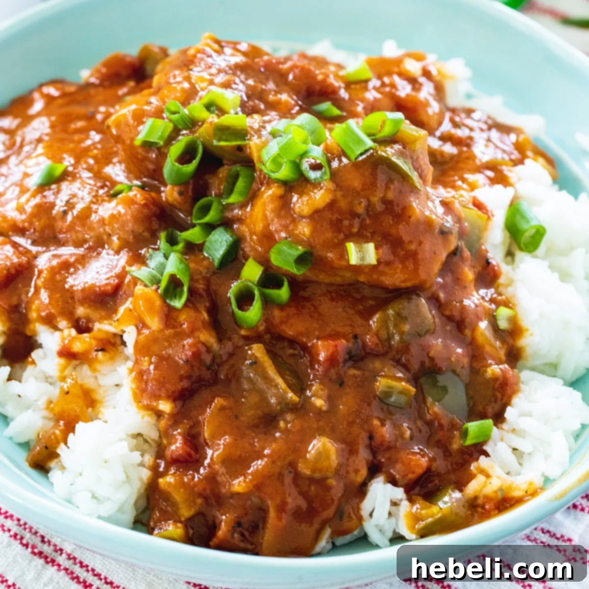 A hearty bowl of Chicken Sauce Piquant served over white rice, garnished with fresh green onions, showcasing its rich texture and vibrant colors.