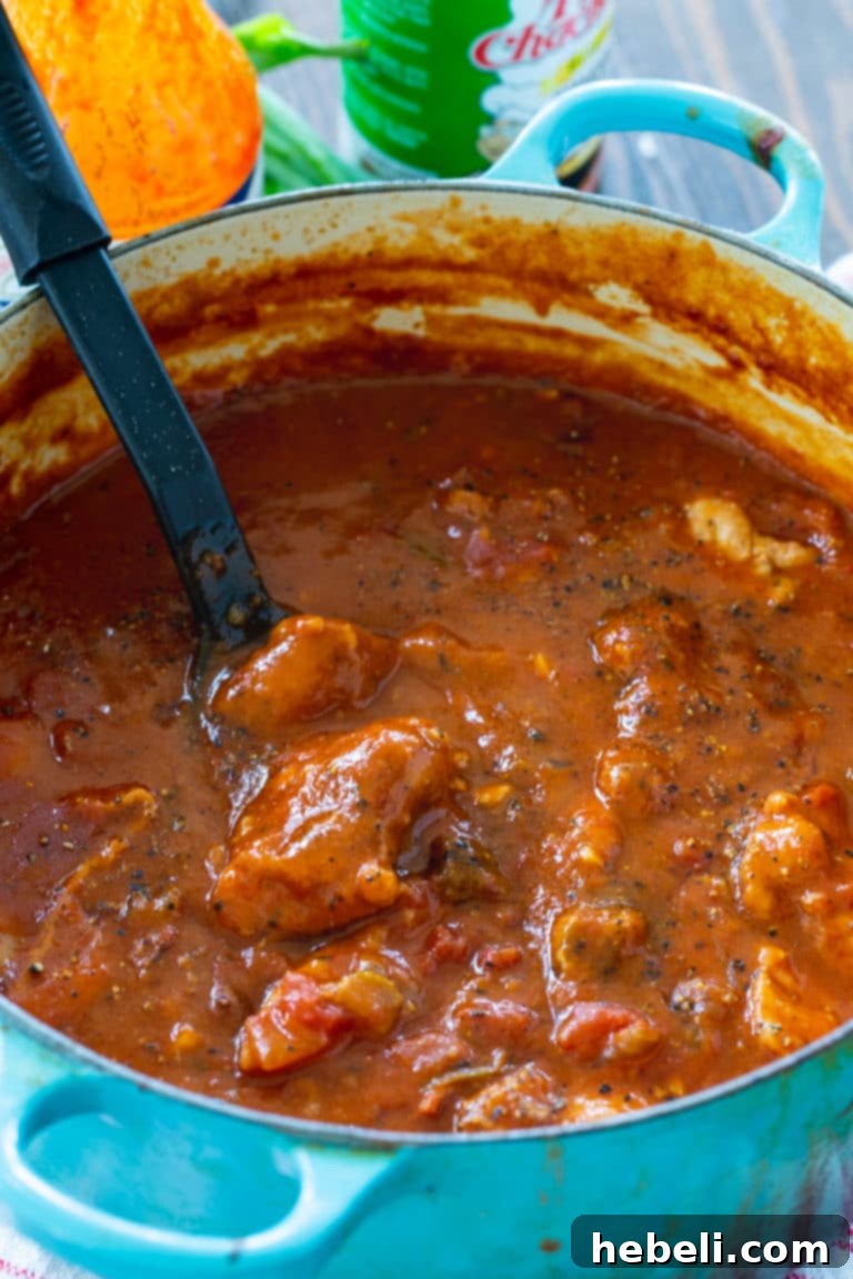 Close-up view of Chicken Sauce Piquant simmering gently in a traditional Dutch oven, highlighting the rich, thick tomato sauce and tender chicken pieces.