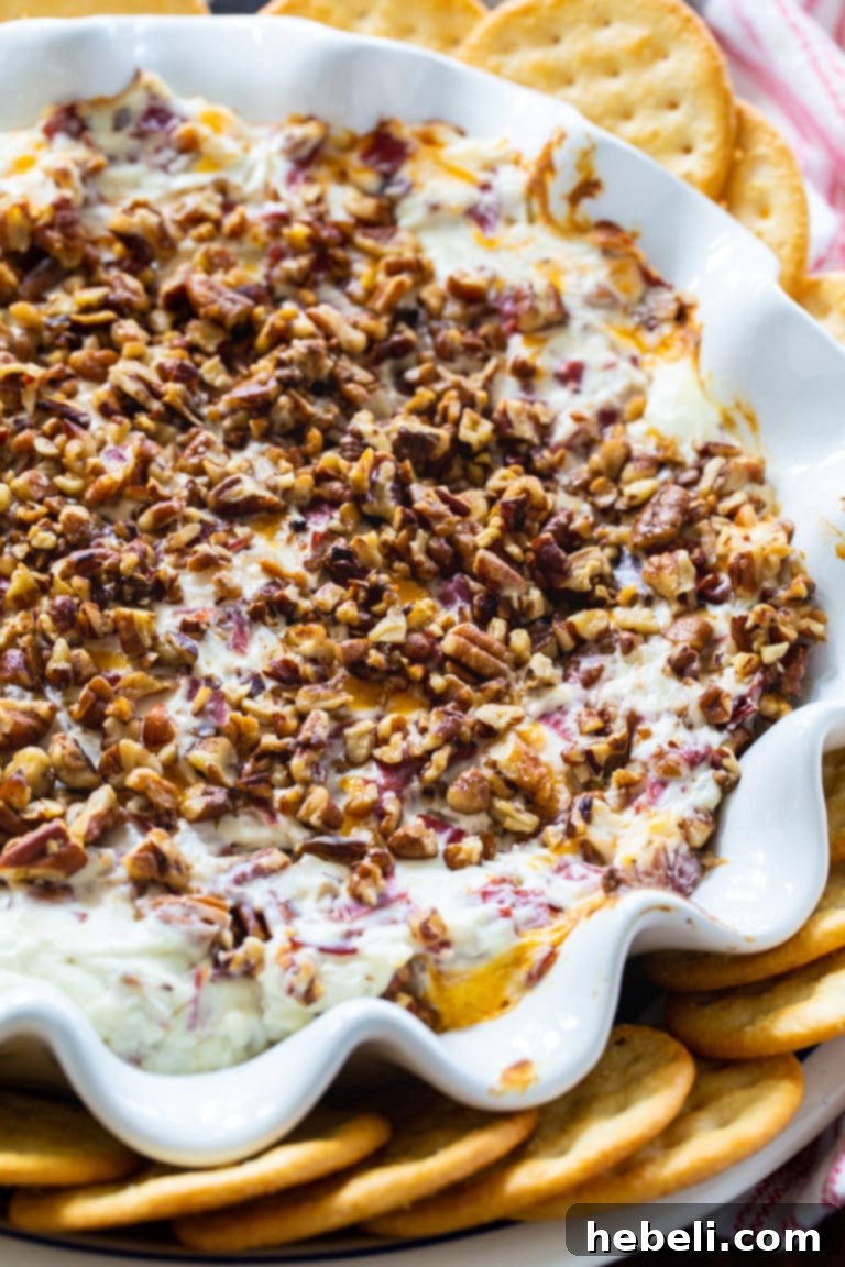 Hot Pecan Beef Dip served on a rustic wooden board with a variety of crackers and greenery.