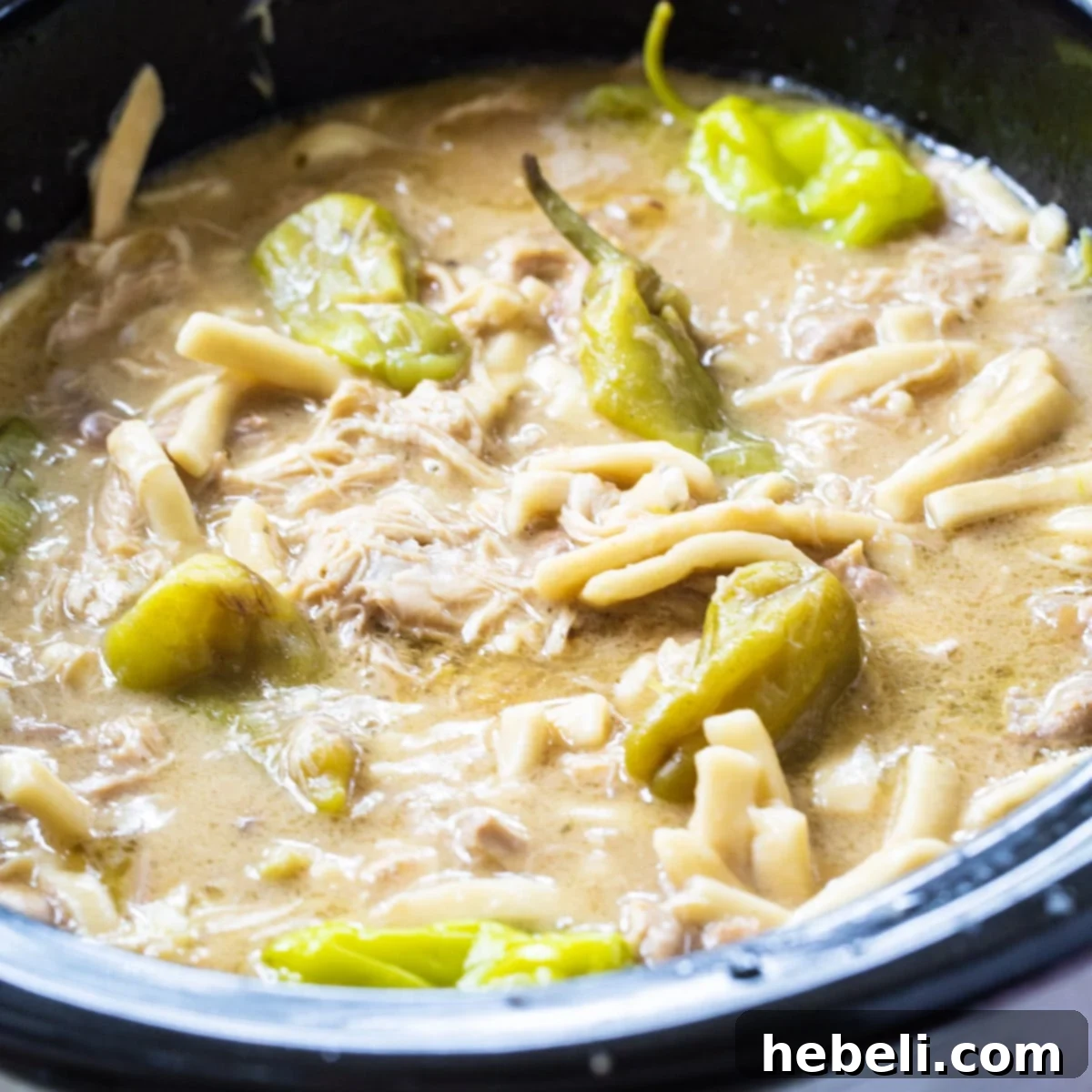 Hearty Crock Pot Mississippi Chicken and Noodles in a black slow cooker, ready to serve.