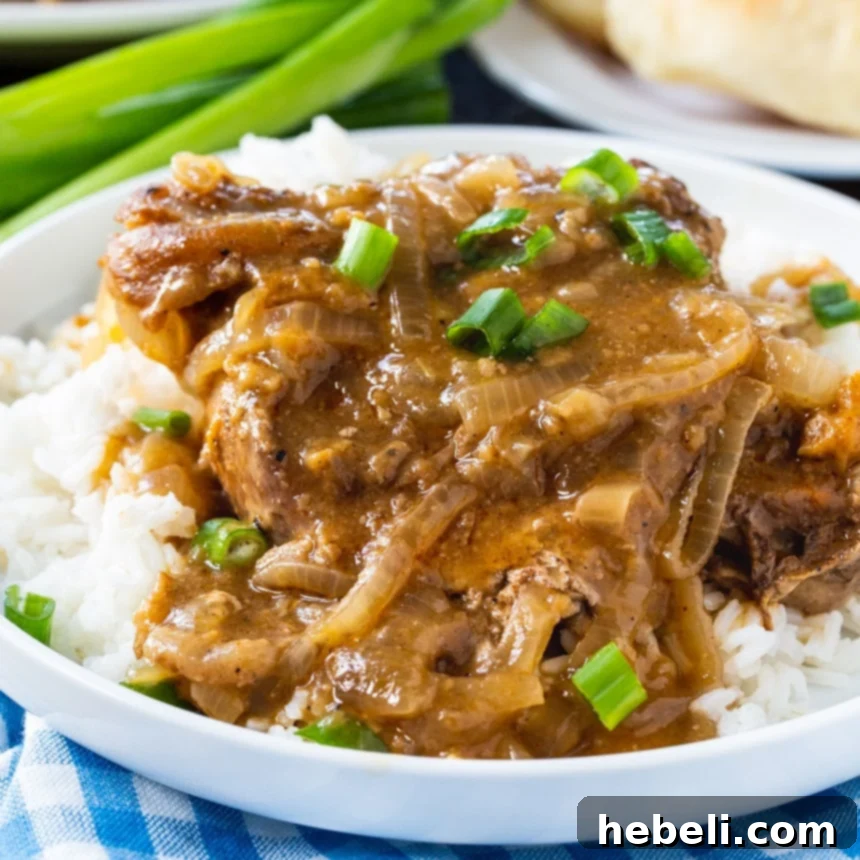Slow Cooker Smothered Pork Chops served over white rice, showcasing the rich, dark gravy and tender onions.