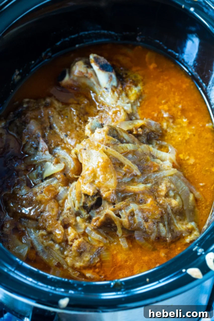 Slow Cooker Smothered Pork Chops cooking in a crock pot, surrounded by a rich, bubbly onion gravy.