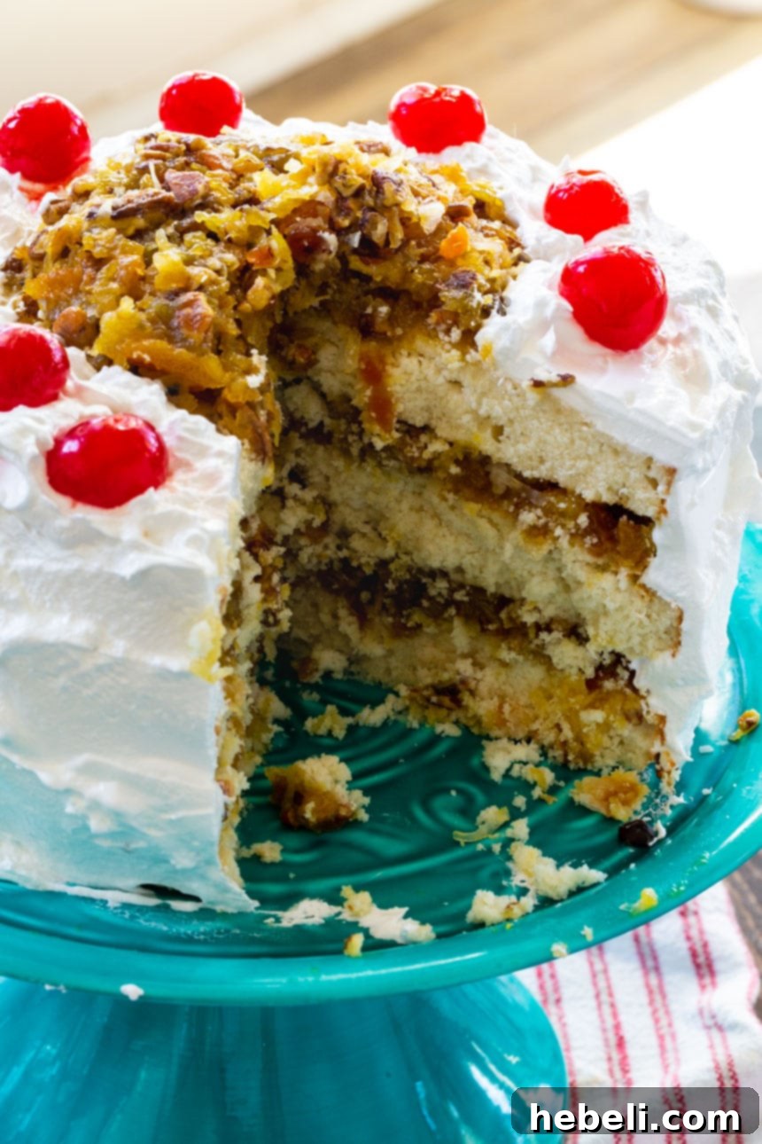 Southern Lane Cake lavishly frosted with pristine white 7-Minute Frosting, providing a sneak peek of the rich fruit, coconut, pecan, and bourbon filling beneath.