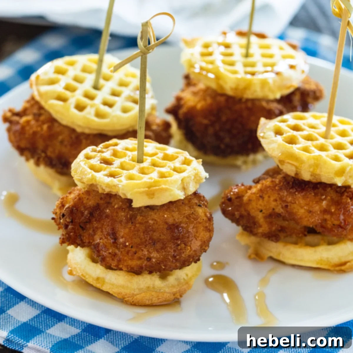 Four perfectly assembled Chicken and Waffle Sliders on a white plate, ready to be served.