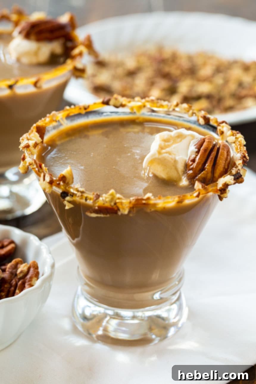 A close-up of a Pecan Pie Martini, highlighting the caramel and pecan rim, with a plate of chopped pecans in the background, suggesting the key flavor.