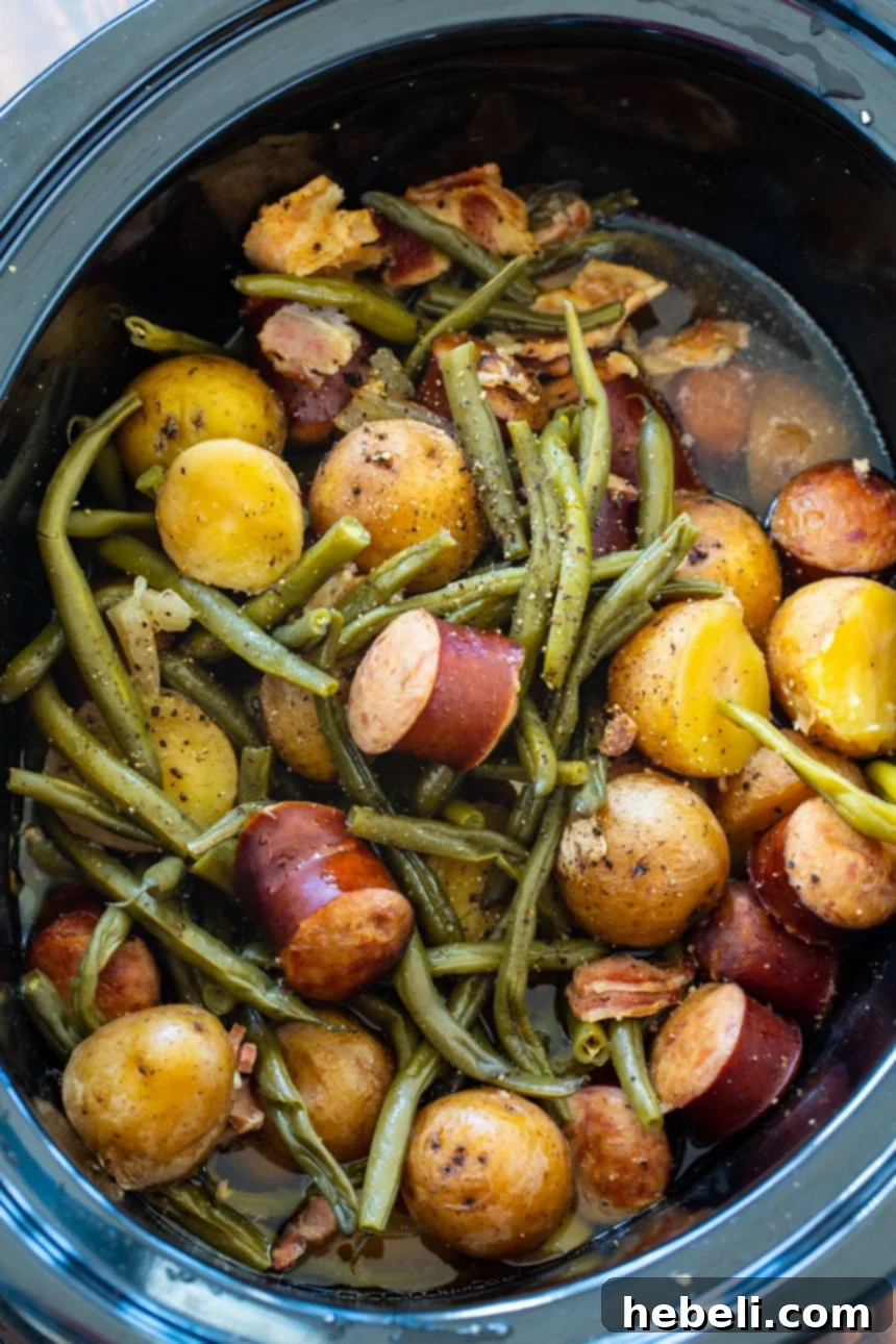 A slow cooker filled to the brim with Crock Pot Sausage, Potatoes, and Green Beans, ready to serve.
