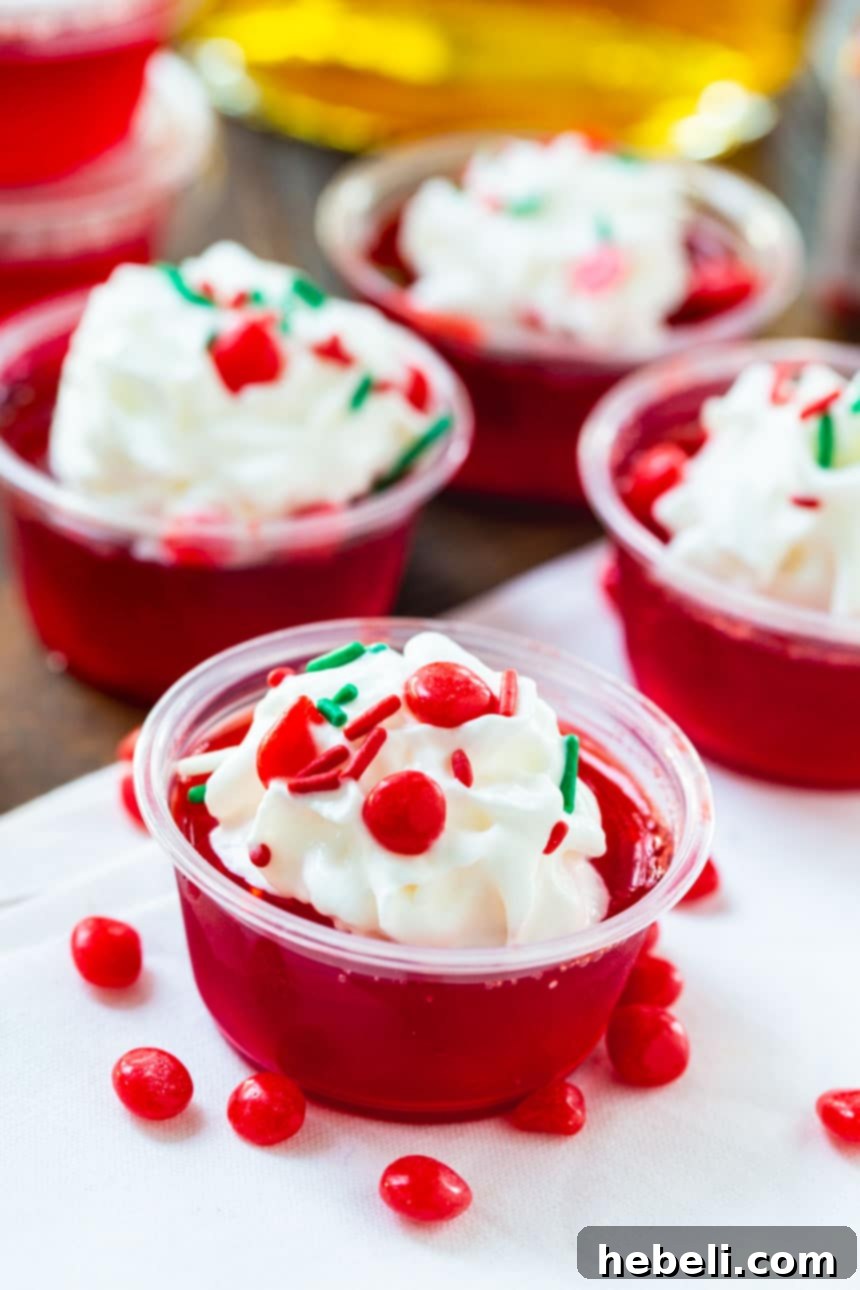 Fireball Jell-O Shots 3 Close-up of Fireball Jello Shots in small cups, topped with whipped cream, sprinkles, and Red Hot candies, against a blurred festive background.
